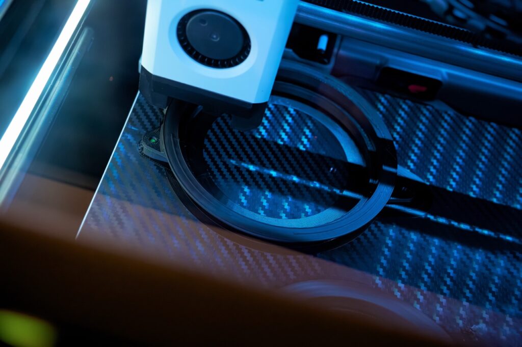 Advanced 3D Printer at Work Creating Precise Components on a Carbon Fiber Surface in a Modern Workshop Environment